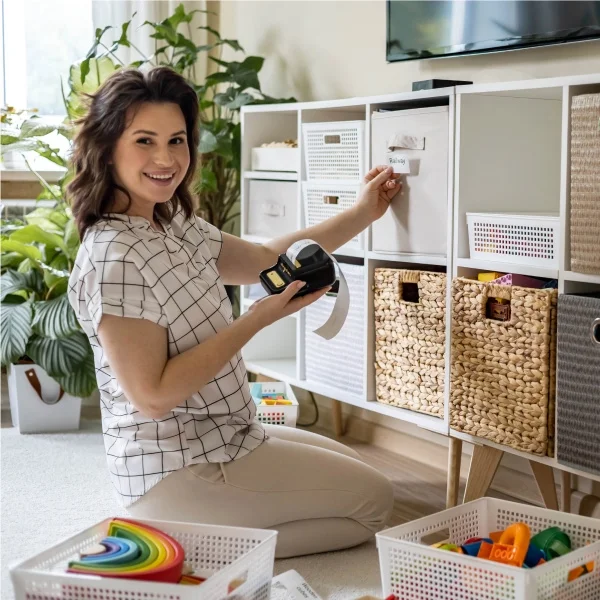 Une femme assise par terre à côté d'une boîte à jouets ouverte, entourée de jouets éparpillés.